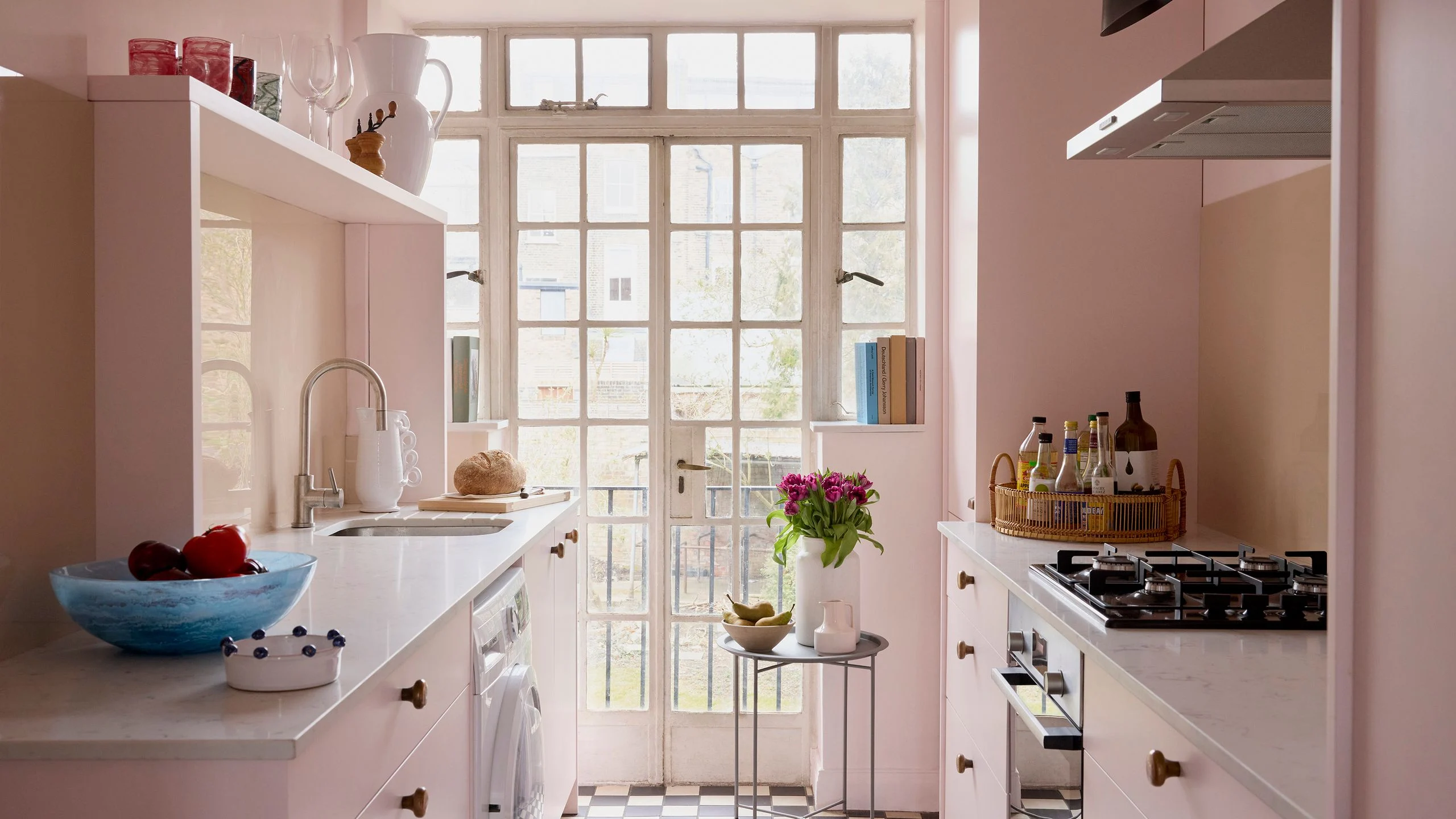 Soft pink galley kitchen with brass knobs and black and white checkerboard floor