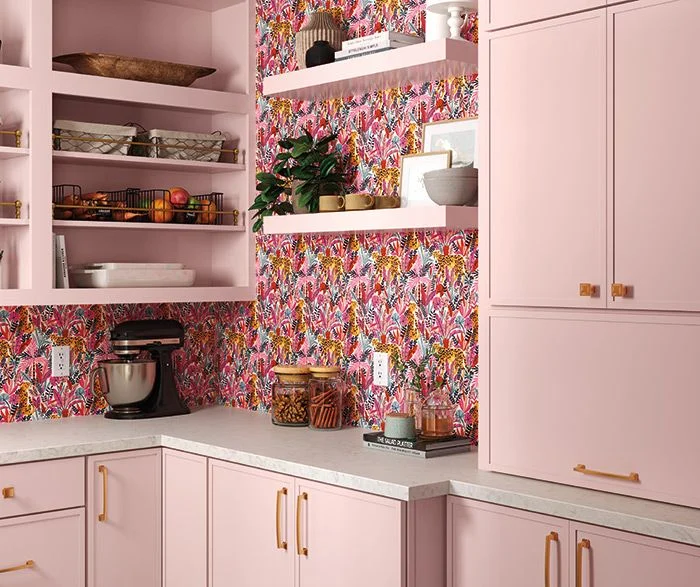 Blush pink pantry cabinets with brass pulls and tropical wallpaper backdrop